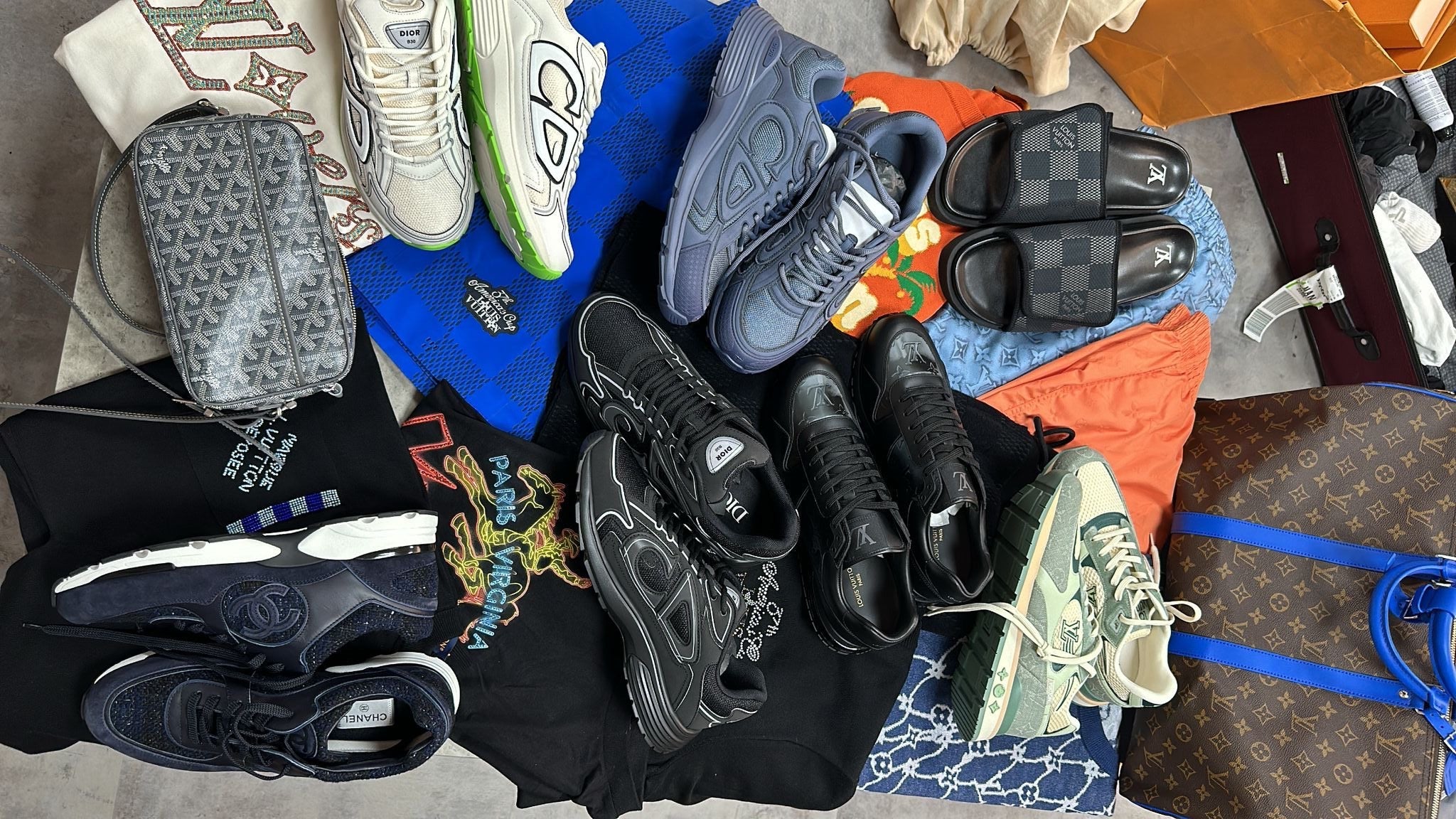 Collection of shoes and clothing on a textured surface with a Louis Vuitton bag.